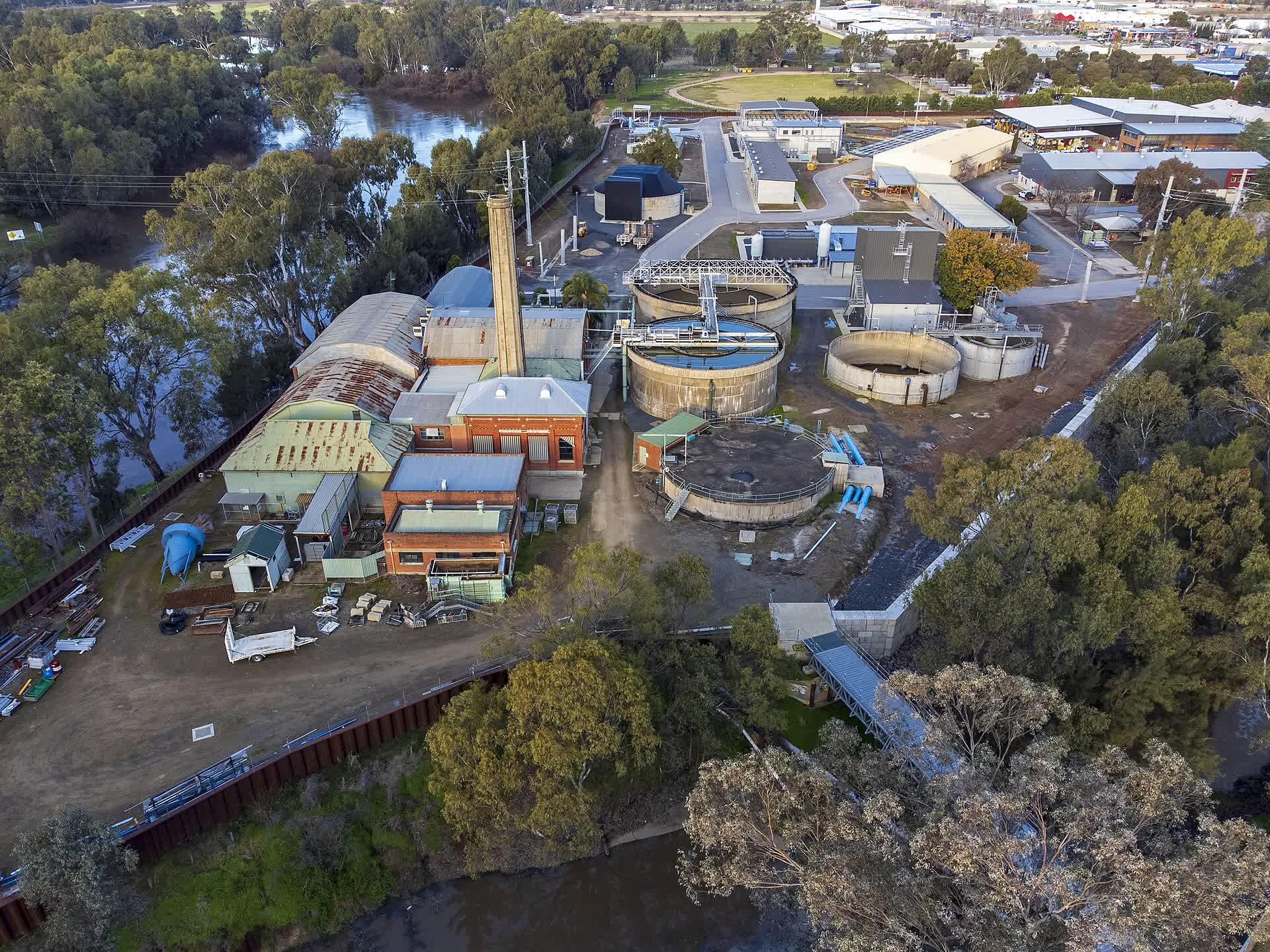 Aerial view of the Wagga Wagga water treatment plant, with round settling tanks and buildings beside a river lined with gum trees