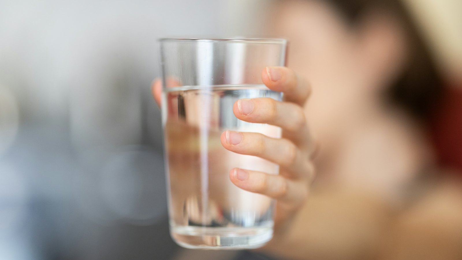 A hand holding a clear glass of water