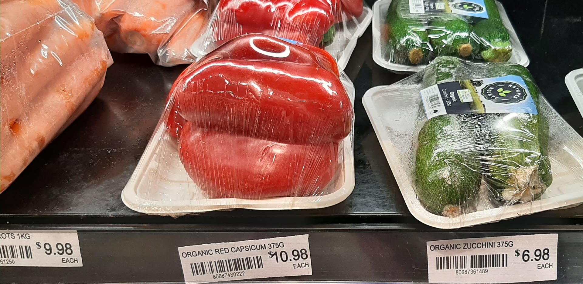 Shelf price tags in an Australian shop: organic red capsicum $10.98 each and organic zucchini $6.98 each